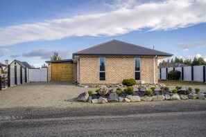 A single-story brick house with a sloped roof, a front garage door, and a gravel driveway.