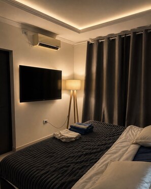 A hotel room with a bed, a flat-screen TV mounted on the wall, a standing lamp, and a window with dark curtains. - Family Room (Foz do Iguaçu)