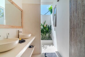 Um banheiro moderno com um espelho grande, duas pias e uma pequena janela com plantas.