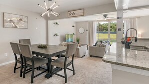 A dining area with a dark wooden table and chairs, a ceiling fan, and a kitchen area with a granite countertop. - Spacious 3-bedroom apartment near Disney (Davenport)