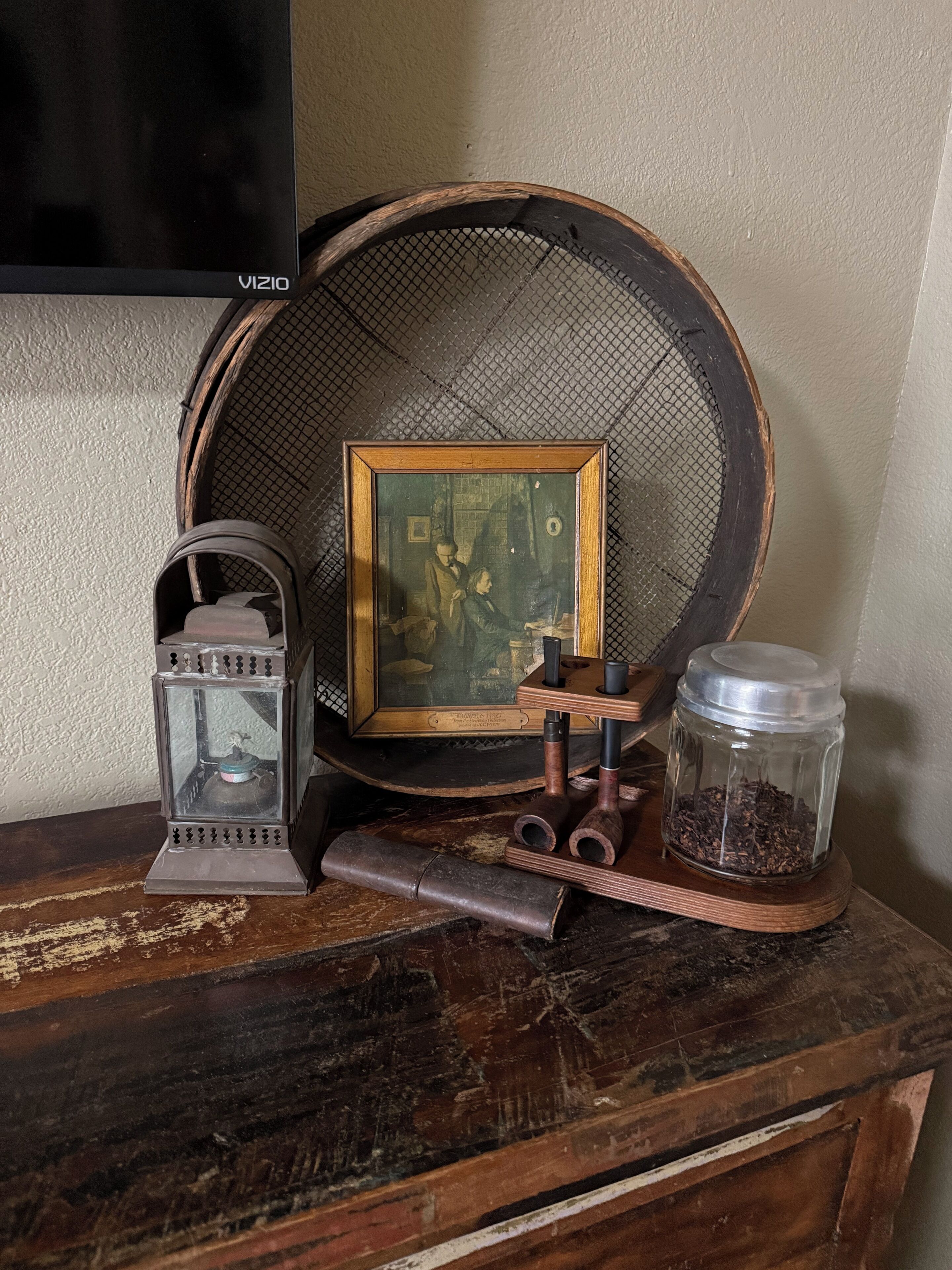 Een houten tafel in vintage-stijl met een lijstwerk schilderij, een oude lantaarn en een glazen pot gevuld met een donkere substantie.