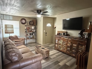 A living room with a sofa, a wooden cabinet, a television, and a ceiling fan.