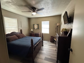 Une chambre à coucher comprenant un lit, un ventilateur de plafond, une commode et un téléviseur fixé au mur.