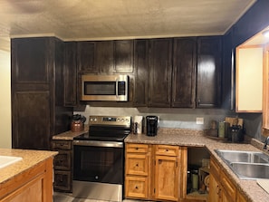 A kitchen with dark wooden cabinets, a stainless steel microwave, a stove, and a sink.