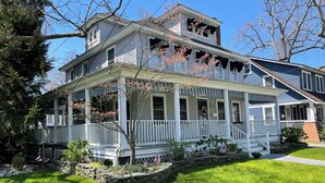 A two-story house with a porch, stone wall, and American flags. - Beach Retreat w/ Hot Tub, Wraparound Porch, beach passes, bikes - Sleeps 12 (Bradley Beach)