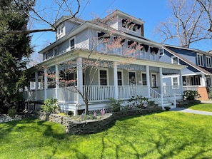 Ein zweistöckiges Haus mit Veranda, Steinmauer und amerikanischen Flaggen.