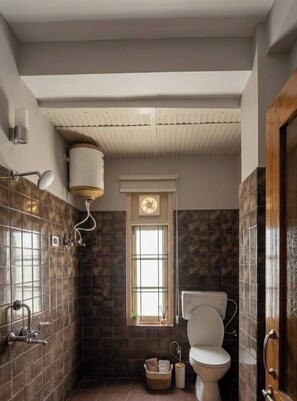 A bathroom with a toilet, a shower, a window, and a wall-mounted toilet paper holder.
