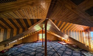 An attic room with wooden beams, patterned rugs, and a large window.