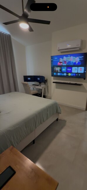 A hotel room with a bed, a desk with a computer, a television mounted on the wall, and a ceiling fan. - Beautiful 3-bed house,came and discover the beauty of casa Valencia. (Hermosillo)