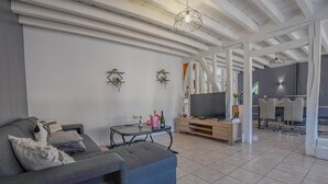 Un salon moderne avec un canapé gris, un téléviseur posé sur un meuble en bois et un coin repas comprenant des chaises et une table.
