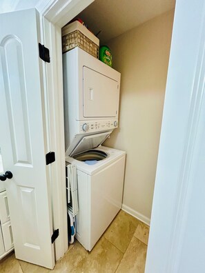 Un lavadero pequeño y funcional con lavadora y secadora apiladas, una puerta y un espacio de almacenamiento sobre la secadora.