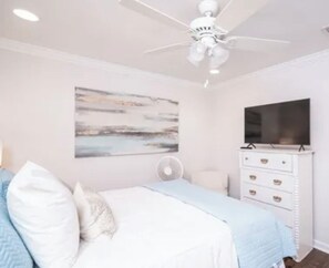 A bedroom with a bed, a ceiling fan, a dresser, a TV, and a wall art piece.