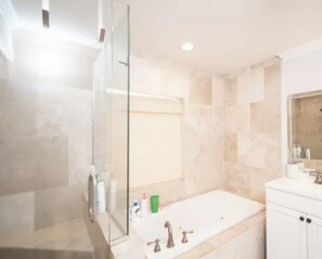 A modern bathroom with a glass shower enclosure, a freestanding bathtub, and a vanity with a mirror.