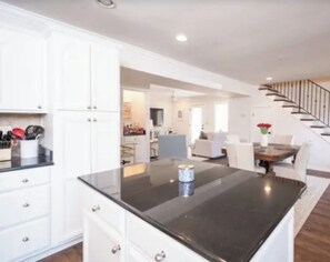 A modern kitchen with white cabinetry, a black countertop, and a dining area with a wooden table and white chairs.