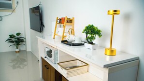 Ett modernt kök med en vit bänkskiva, en trästege, en liten krukväxt, en guldfärgad golvlampa och en tv som är monterad på väggen.