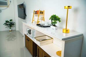 A modern kitchen with a white countertop, a wooden ladder, a small potted plant, a gold floor lamp, and a television mounted on the wall. -  PRIME LOCATION • NEW 1BR CONDO FOR RENT (Lapu-Lapu)