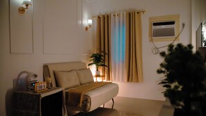 Ett sovrum med en säng, ett sängbord, en lampa, gardiner och ett fönster med en luftkonditioneringsenhet.