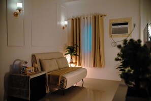 A bedroom with a bed, bedside table, lamp, curtains, and a window with an air conditioning unit. -  PRIME LOCATION • NEW 1BR CONDO FOR RENT (Lapu-Lapu)