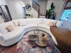 A modern living room with a curved white sectional sofa, a coffee table with a vase and a book, and a large plant. -  Spacious 5-bedroom, 2 kitchens, 2 master bedrooms with a finished basement. (Austell)
