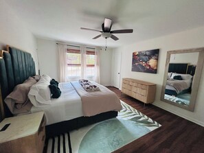 A bedroom with a bed, a ceiling fan, a dresser, a mirror, and a window with curtains. -  Spacious 5-bedroom, 2 kitchens, 2 master bedrooms with a finished basement. (Austell)
