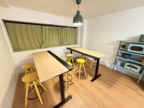 A room with a wooden floor, a table with chairs, a shelf with kitchen appliances, and a window with curtains. - KANDA URBAN SUITES (Chiyodaku Uchikanda)