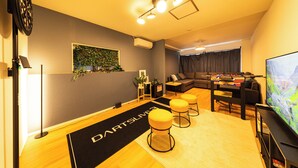 A modern living room with a dartboard, a sofa, a coffee table, and a television. - KANDA URBAN SUITES (Chiyodaku Uchikanda)