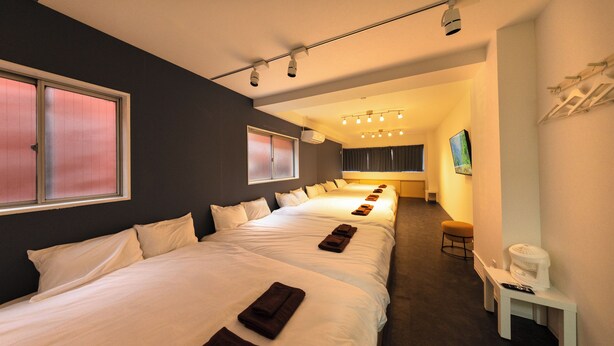 A hotel room with multiple beds, a small table, a chair, and a television. - KANDA URBAN SUITES (Chiyodaku Uchikanda)
