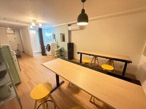 A room with a long table, two yellow stools, a washing machine, and a ceiling light fixture. - KANDA URBAN SUITES (Chiyodaku Uchikanda)