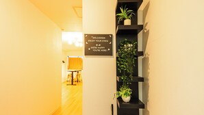 A hallway with wooden flooring, a black wall-mounted shelf with plants, and a welcome sign. - KANDA URBAN SUITES (Chiyodaku Uchikanda)