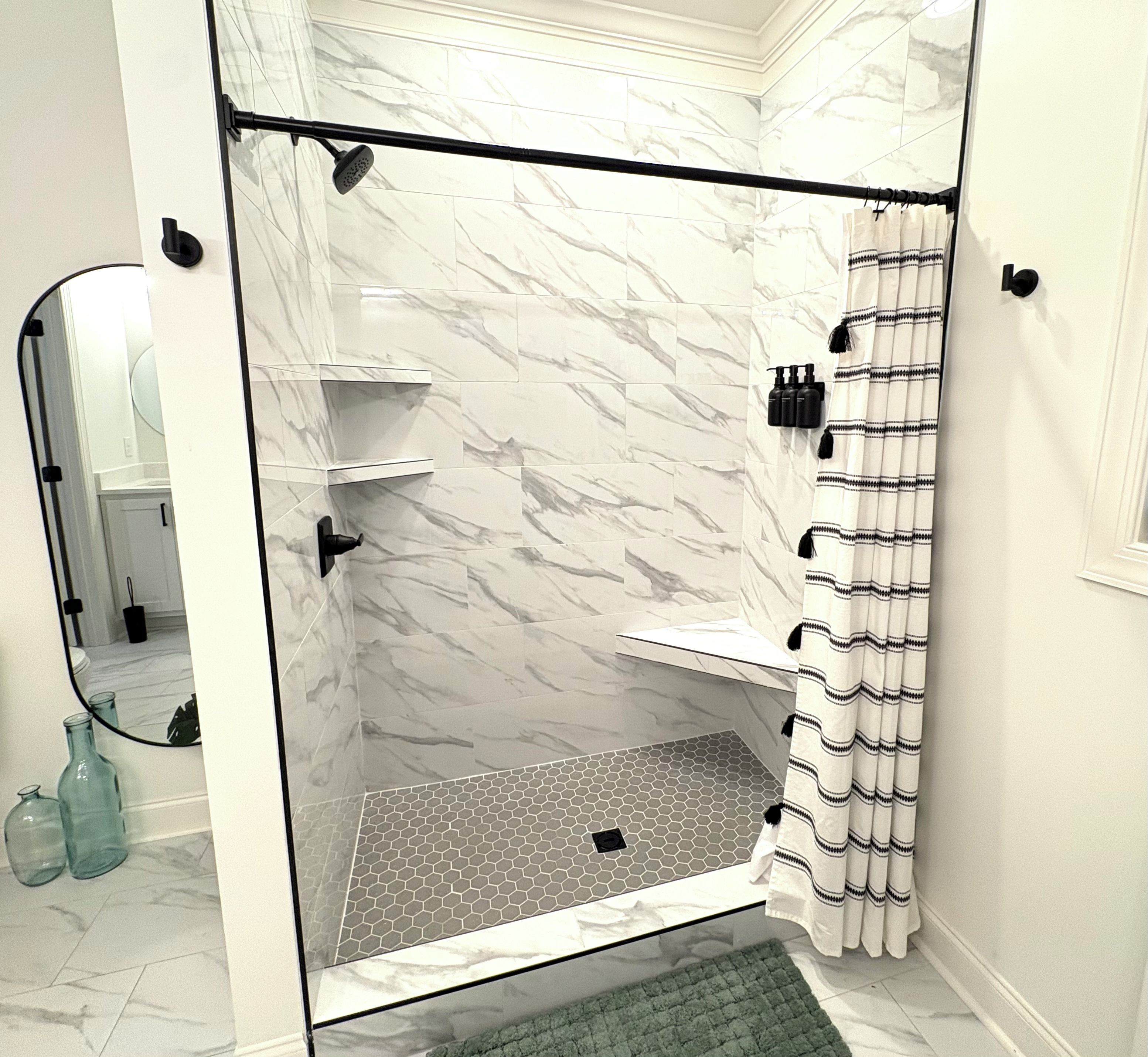 A glass-enclosed shower with marble walls, a hexagonal tile floor, and a shower curtain with tassels.