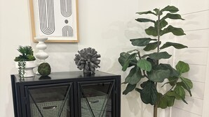 Et sort metalskab med glasdøre, en potteplante og et indrammet kunstværk på væggen.