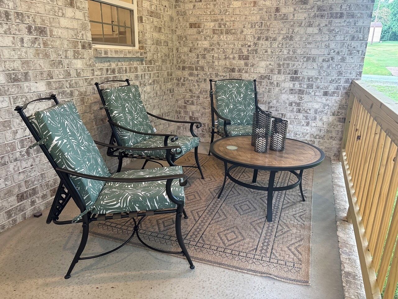 Une terrasse avec trois chaises et une table, un tapis à motifs et un mur en briques.