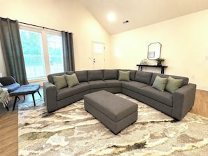 A living room with a sectional sofa, ottoman, and a patterned rug.
