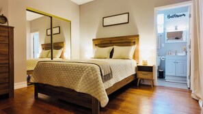 A bedroom with a large bed, bedside tables, a mirror, and a bathroom sign. - Cozy modern studio (Tampa)
