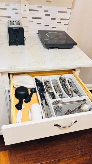 A kitchen counter with a Hamilton Beach toaster and a Karinaor induction cooktop. Below, a drawer contains a variety of kitchen utensils. - Cozy modern studio (Tampa)