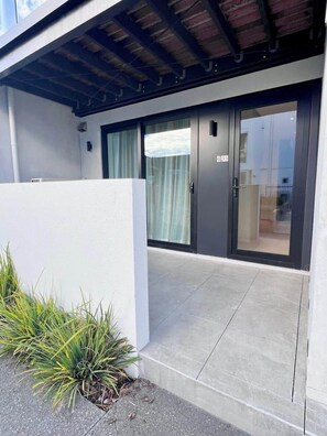 A modern building with a glass door entrance, a concrete pathway, and a small garden area with plants. - Best Location in City Centre-Free parking (Christchurch)