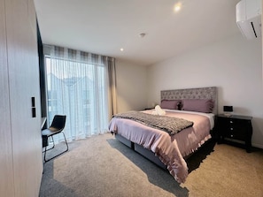 Ein modernes Schlafzimmer mit einem großen Bett, einem Sessel, einem Nachttisch und einem Fenster mit Vorhängen.