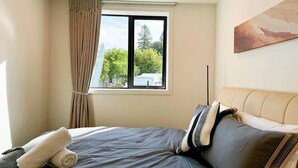 A bedroom with a bed, a window with curtains, a painting on the wall, and a view of trees and a car outside. - Queenstown Garden - Lake View (Queenstown)