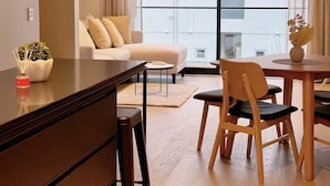 Una sala de estar moderna con un sofá, una mesa de comedor con sillas, una mesa de centro y un ventanal con cortinas.