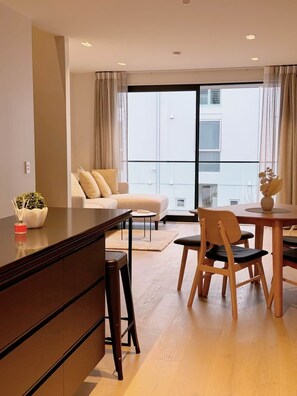 Ein modernes Wohnzimmer mit einer Couch, einem Esstisch mit Stühlen, einem Couchtisch und einem großen Fenster mit Vorhängen.