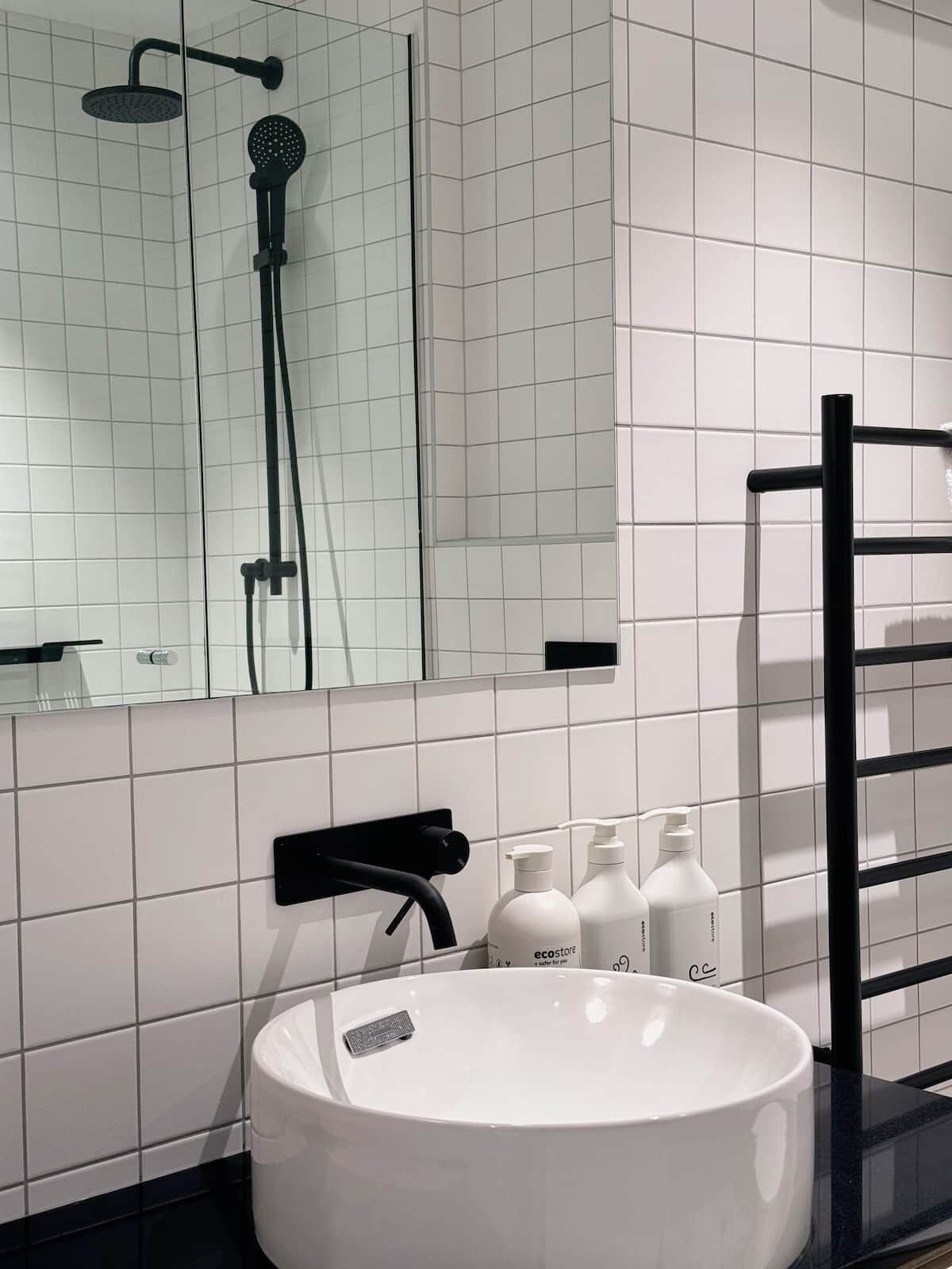 A bathroom with a white sink, black towel rack, and a mirror above the sink.