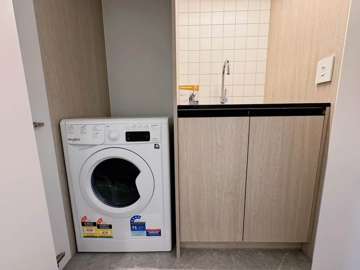 Een praktische wasruimte met een voorlader wasmachine van Whirlpool, een wasbak en een kast.