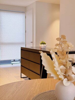 Ein modernes Interieur mit einem Holztisch, einer weißen Vase mit Blumen, einem kleinen Topfpflanzen und einer dunkelbraunen Kommode.