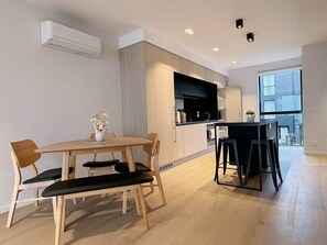 A modern kitchen with wooden cabinets, a dining area with a wooden table and chairs, and a large window providing natural light. - Central Christchurch Apartment-Free Parking (Christchurch)
