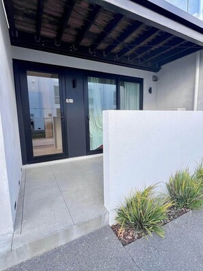 A modern building entrance with a glass door, a concrete pathway, and a small garden area with plants. - Central City Garden - Free Parking (Christchurch)