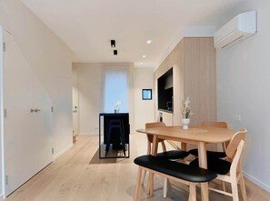 Eine moderne Küche mit Einbauofen, ein Essbereich mit Holztisch und -stühlen sowie ein Flur, der zum Schlafzimmer führt.