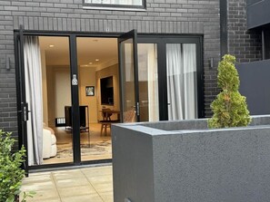 Un edificio moderno con entrada de puerta corredera de vidrio, una planta de interior pequeña y una habitación visible con sofá y televisor.