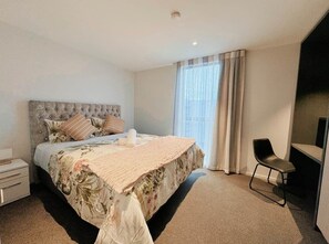 Un dormitorio con cama, una silla, una mesita de noche y una ventana con cortinas.