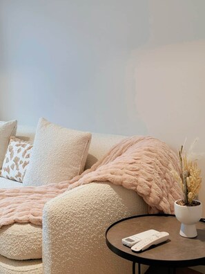 Ein gemütliches Wohnzimmer mit einer Couch, einem runden Couchtisch mit Fernbedienung und einer Zierpflanze.