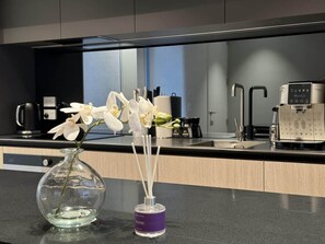 Eine moderne Küche mit Kaffeemaschine, Blumen in einer Vase und einem kleinen violetten Behälter.